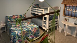 A child's bunk bed with a hammock in a room with a ceiling fan, a small table, and a window with a view of the ocean.