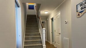 A carpeted staircase with a handrail, a door with a sign reading "Welcome to the Beach," and a vent on the wall.