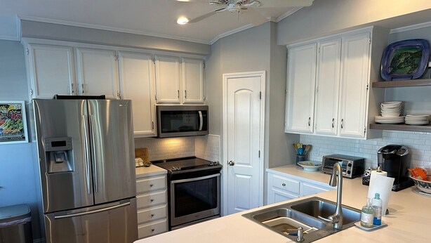 A modern kitchen with white cabinetry, stainless steel appliances, and a large island with a sink.