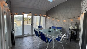A covered patio with a glass table and blue chairs, string lights, and a lantern on a small table.