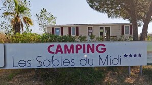 Señal de un camping llamado 'Les Sables du Midi' con un edificio al fondo.