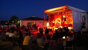Un escenario al aire libre con una banda tocando, rodeado de invitados sentados.