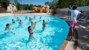Una piscina con gente disfrutando del agua, un tobogán al fondo y sillas de descanso junto a la piscina.