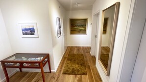 A hallway with wooden flooring, a glass-top table with magazines, and framed pictures on the walls. - Charming & central living in Weiden - Hej (Weiden in der Oberpfalz)
