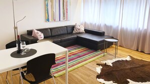 A modern living room with a sectional sofa, a small table, a colorful striped rug, and a cowhide rug. - Charming & central living in Weiden - Hej (Weiden in der Oberpfalz)