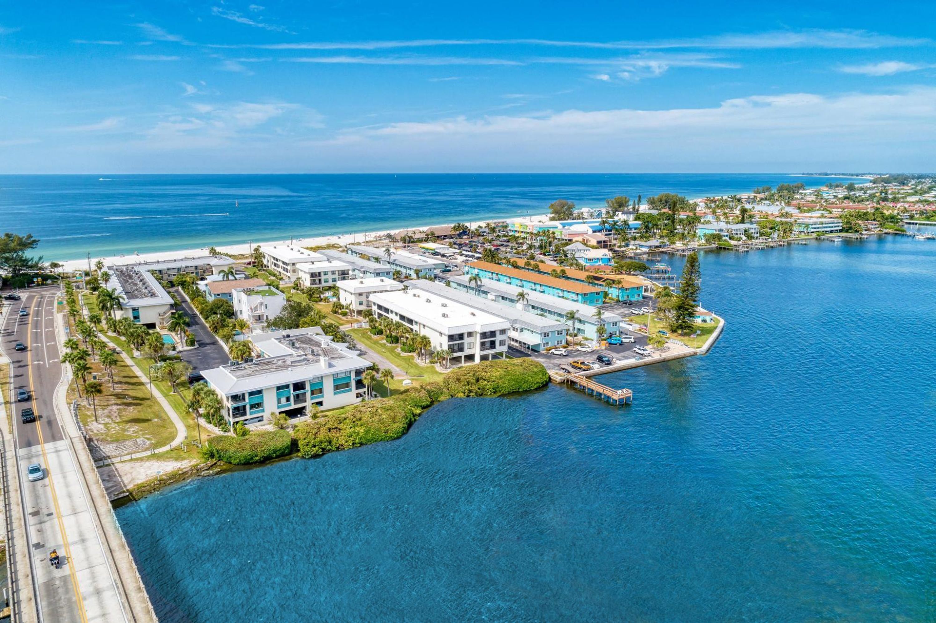 An aerial view of a coastal area with buildings, a marina, and a road.