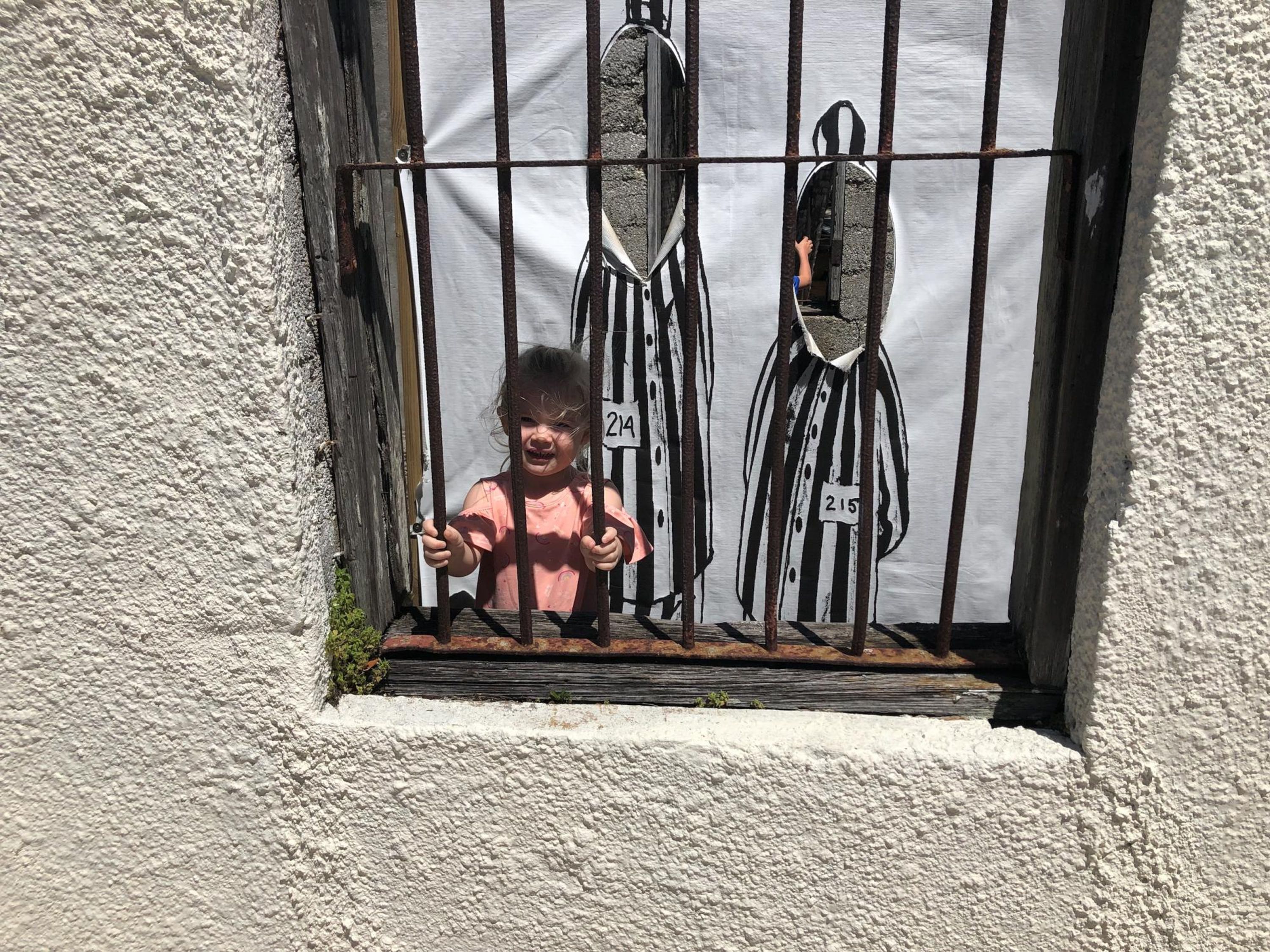 A child in a pink shirt behind a metal gate with numbers 215 and 216 visible.