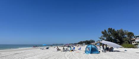 Una spiaggia con una tenda, ombrelloni e lettini.