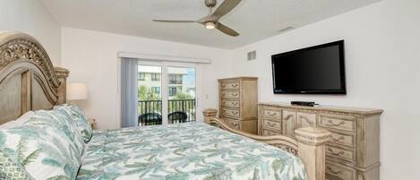 Un dormitorio con cama, ventilador de techo, cómoda, televisor y ventana con vistas a edificios.