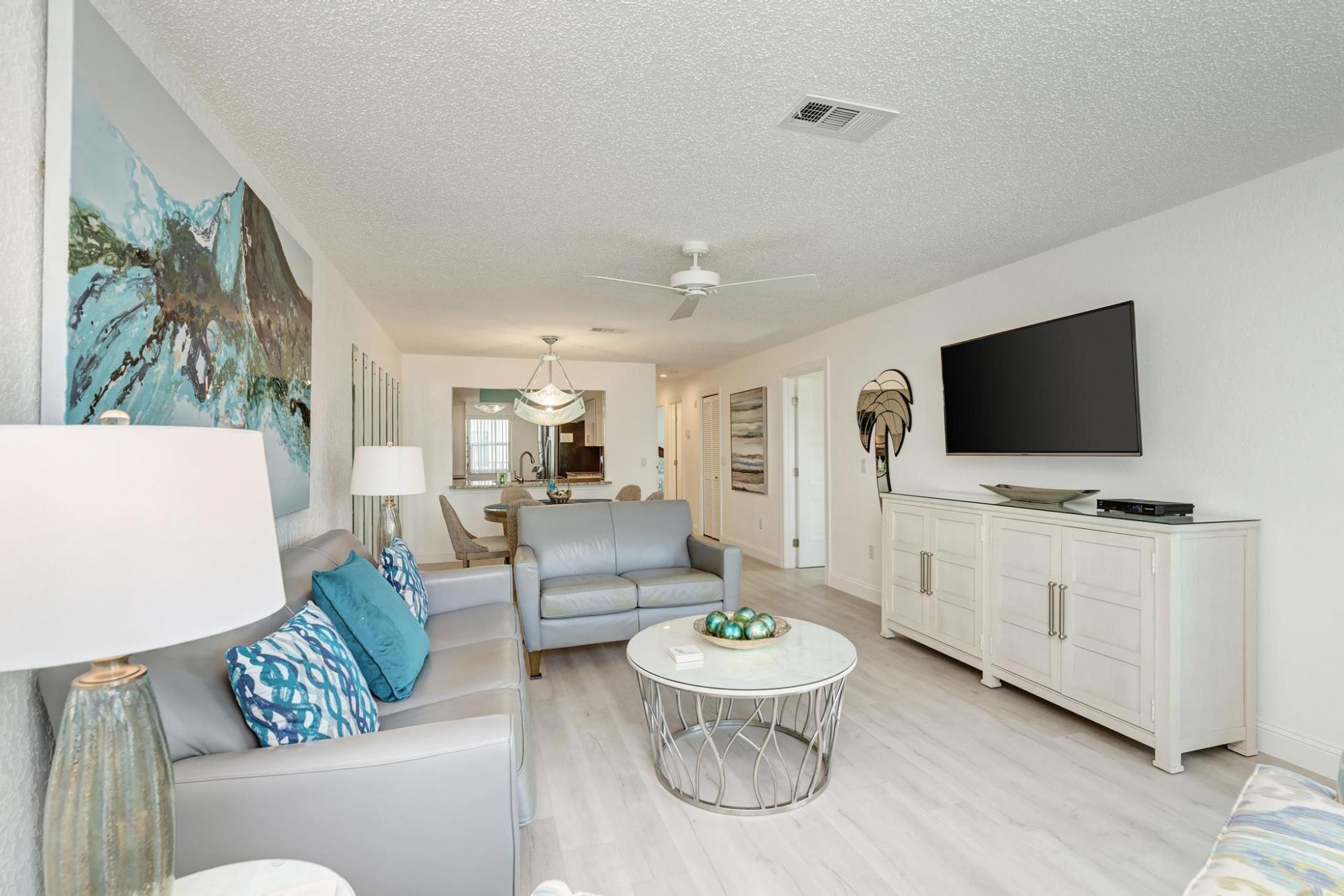 A modern living room with a grey sofa, a round coffee table, and a flat-screen TV on a white cabinet.