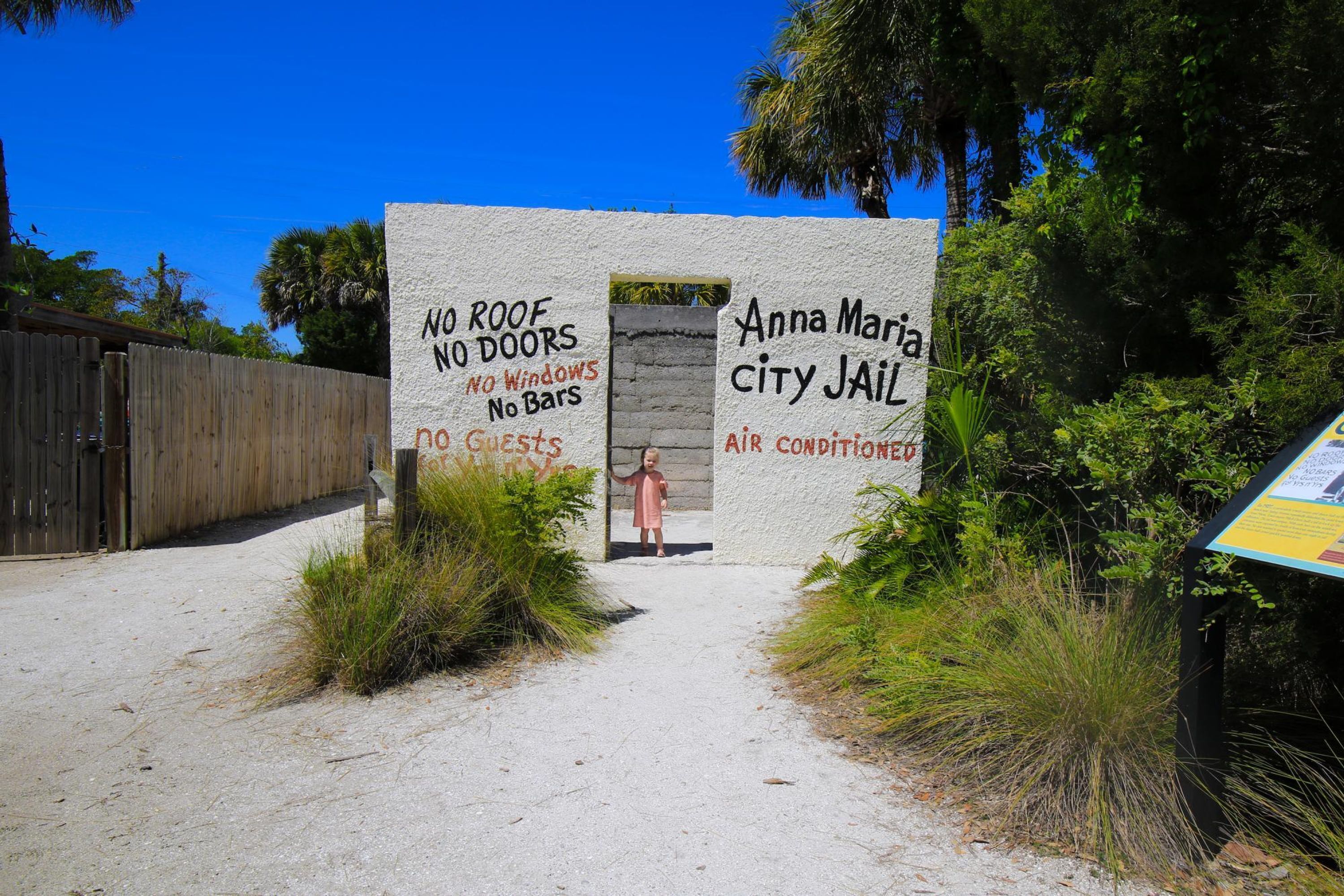 Un muro con grafiti que dice "SIN TECHO, SIN PUERTAS, SIN VENTANAS, SIN JAULAS, SIN HUESPEDES" y "Cárcel Municipal de Anna Maria, CON AIRE ACONDICIONADO".