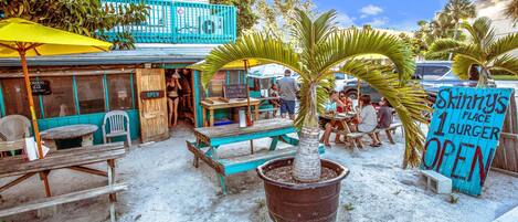 An outdoor dining area with wooden tables and benches, a large potted palm tree, and a sign advertising a burger place.