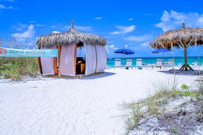 Een wellnesscentrum aan het strand, met een rieten gebouw, ligstoelen en een helder uitzicht op de oceaan.