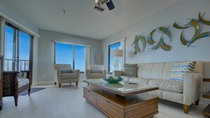 A spacious living room with a large window, a white sofa, two armchairs, and a wooden coffee table. - Anna Maria Island Beach Sands (Bradenton Beach)