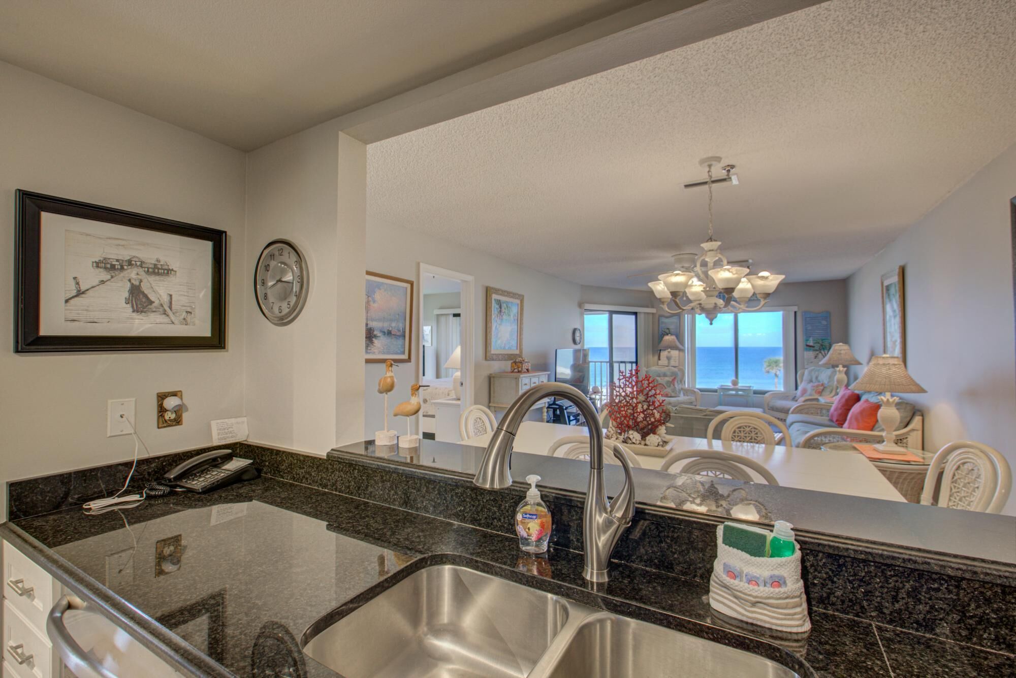 A kitchen with a granite countertop, stainless steel sink, and a view into the living area.