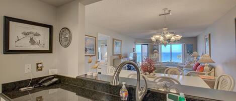A kitchen with a granite countertop, stainless steel sink, and a view into the living area.