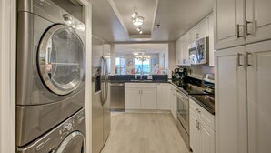 A modern kitchen with stainless steel appliances, white cabinetry, and a central island. - Anna Maria Island Beach Sands 201 (Bradenton Beach)