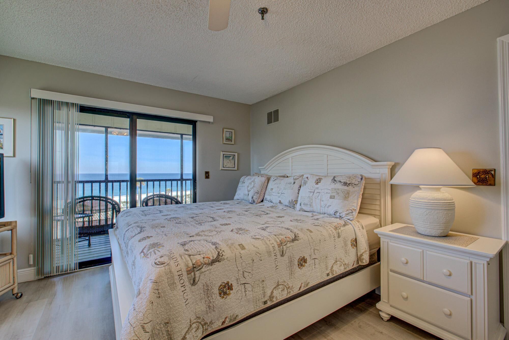 A bedroom with a bed, a nightstand, a lamp, and a view of the ocean through a sliding door.
