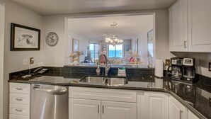 A modern kitchen with a granite countertop, stainless steel appliances, and white cabinetry. - Anna Maria Island Beach Sands 201 (Bradenton Beach)