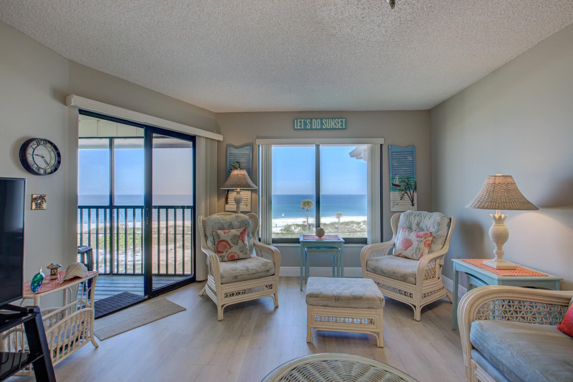 A living room with wicker furniture, a TV, and a view of the beach.