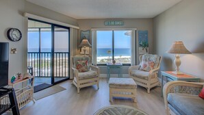 A living room with wicker furniture, a TV, and a view of the beach. - Anna Maria Island Beach Sands 201 (Bradenton Beach)