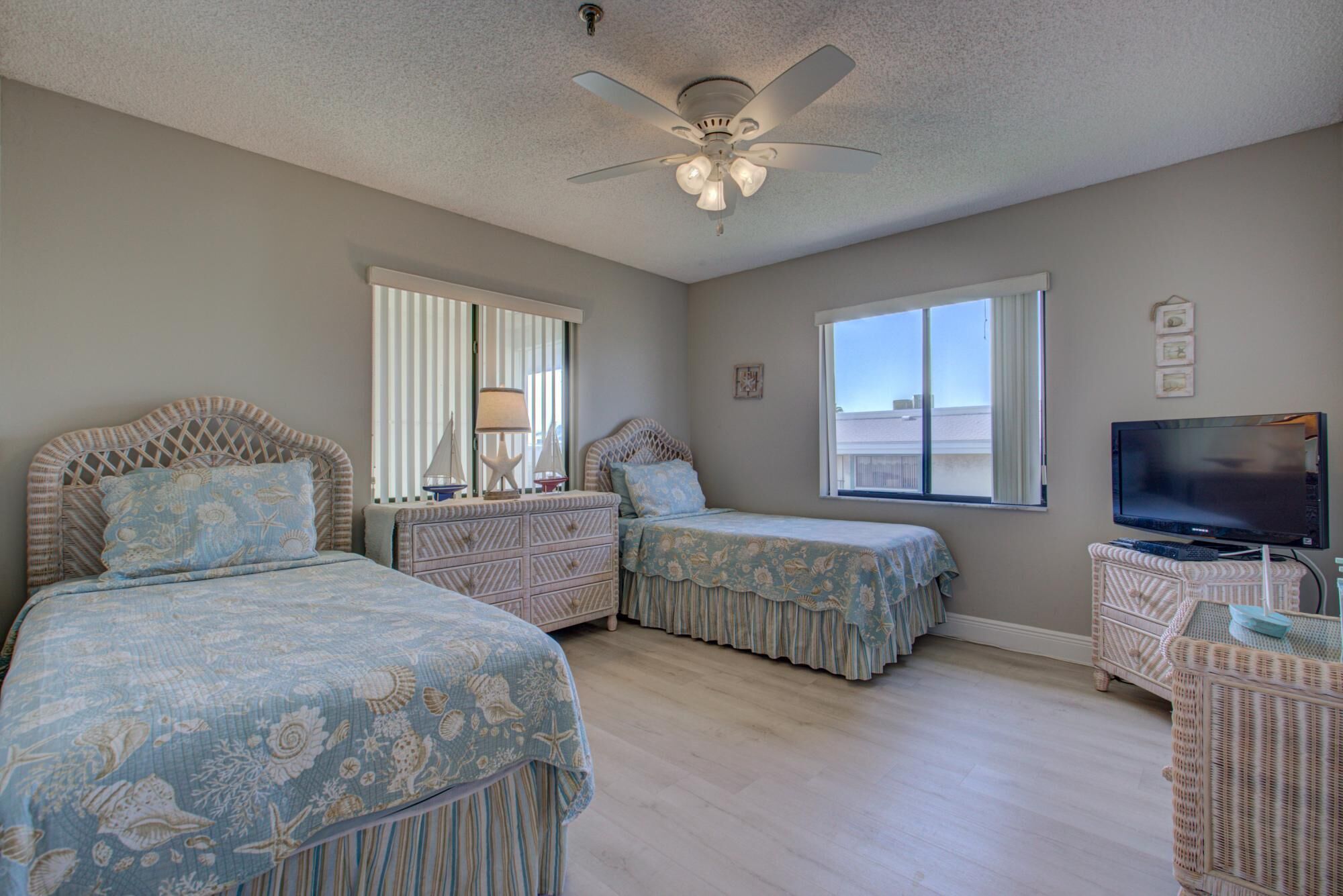 A bedroom with two beds, a ceiling fan, a TV, and a window with a view.