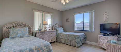 A bedroom with two beds, a ceiling fan, a TV, and a window with a view.