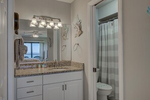 Un baño con encimera de granito, un lavabo blanco, un espejo y una cortina de ducha.
