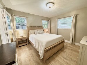 Ein Schlafzimmer mit einem hölzernen Bett, Nachttischen, einem Beistelltisch und einem Fenster mit Vorhängen.