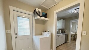 A laundry room with a washer and dryer, a small shelf with a bag, and a kitchen area with cabinets and a sink. - Recently Updated 2/2 With Hot Tub, 1 Mile to Beach (Lantana)