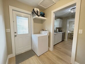 A laundry room with a washer and dryer, a small shelf with a bag, and a kitchen area with cabinets and a sink. - Recently Updated 2/2 With Hot Tub, 1 Mile to Beach (Lantana)