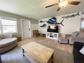 A living room with a flat-screen TV, a ceiling fan, a wooden coffee table, and a sofa.