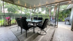 A covered patio area with a table and chairs, surrounded by glass railings and greenery. - Recently Updated 2/2 With Hot Tub, 1 Mile to Beach (Lantana)