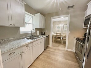 A modern kitchen with a granite countertop, stainless steel appliances, and a dining area with a table and chairs. - Recently Updated 2/2 With Hot Tub, 1 Mile to Beach (Lantana)