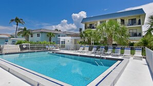 A swimming pool with lounge chairs and palm trees, surrounded by buildings with balconies. - Anna Maria Island Beach Sands 101 (Bradenton Beach)