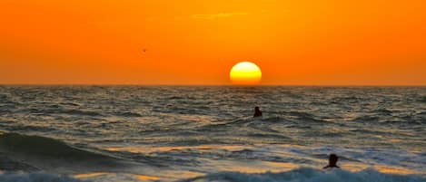 Un atardecer sobre el océano con olas y una persona nadando.