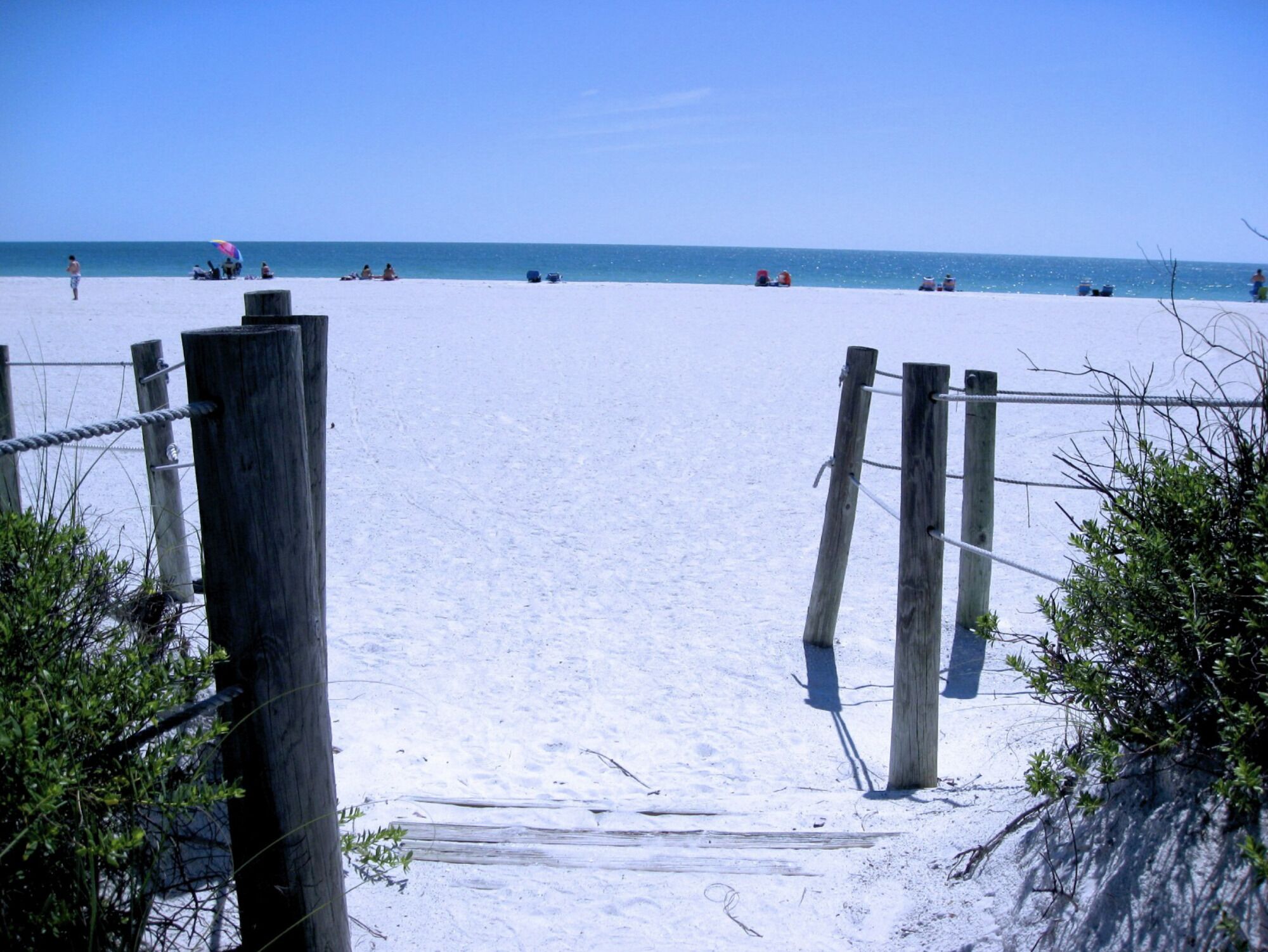 A sandy beach with a wooden fence leading to the water.