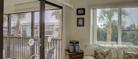 A room with a balcony, a sofa with floral cushions, a clock, and a framed picture on the wall.