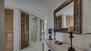 A hallway with wooden doors, a mirror, a lamp, and a small table with a tray. - Anna Maria Island Bridge Port Beach Resort (Bradenton Beach)