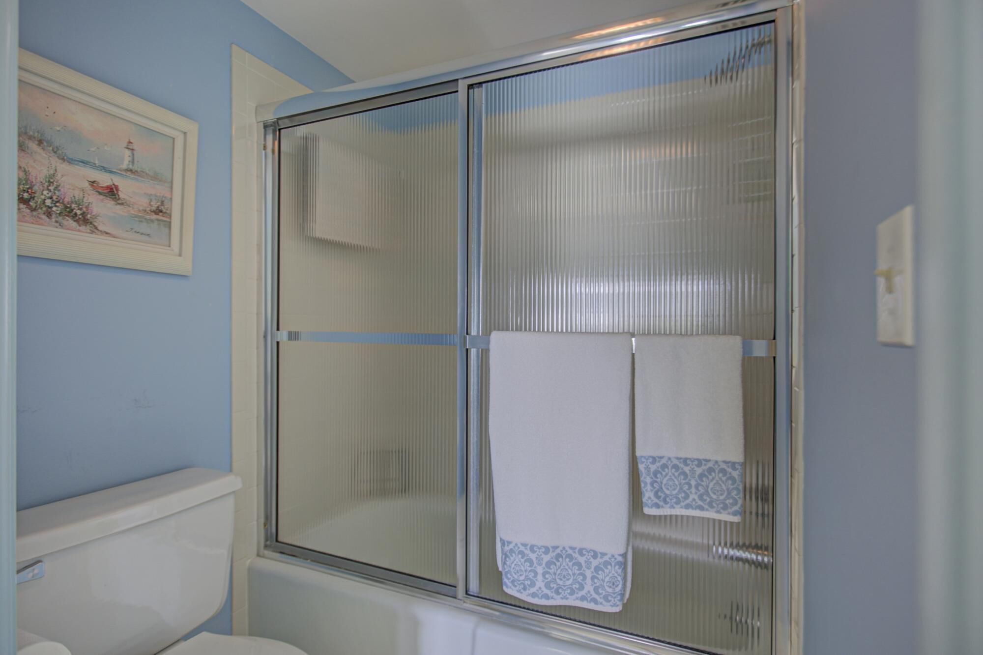 Ein Badezimmer mit Duschkabine aus Glas, Toilette und einem gerahmten Bild an der Wand.