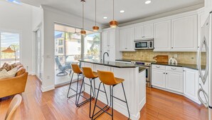 A modern kitchen with white cabinetry, a central island with bar stools, and a view to an outdoor patio.
