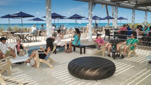 Een terras met tafels, stoelen, parasols en uitzicht op het strand.
