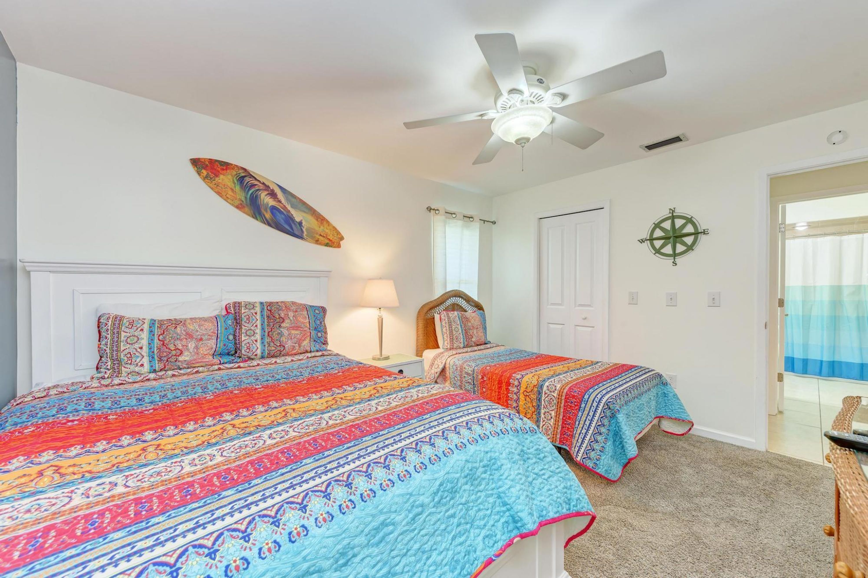 A bedroom with two beds, a ceiling fan, a compass wall decoration, and a window with curtains.