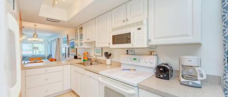 A modern kitchen with white cabinetry, a built-in microwave, a coffee maker, and a dishwasher.