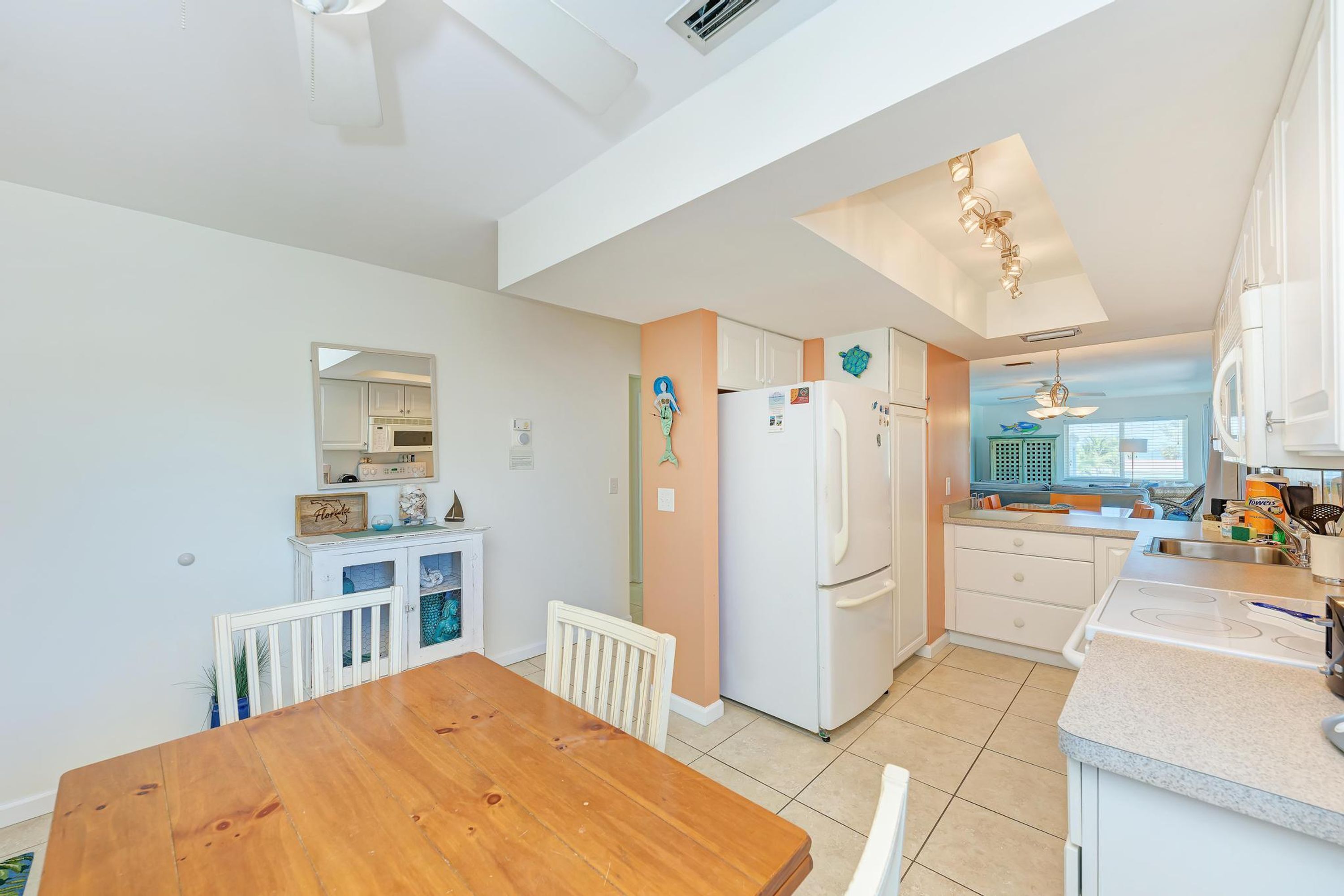 A modern kitchen with white cabinets, a built-in oven, and a white refrigerator. There is a dining area with a wooden table and white chairs.