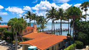 A beachfront property with a red-tiled roof, palm trees, and a dock extending into the water.