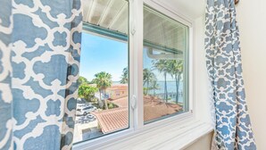 A window with a view of a coastal area, including palm trees and a beach.