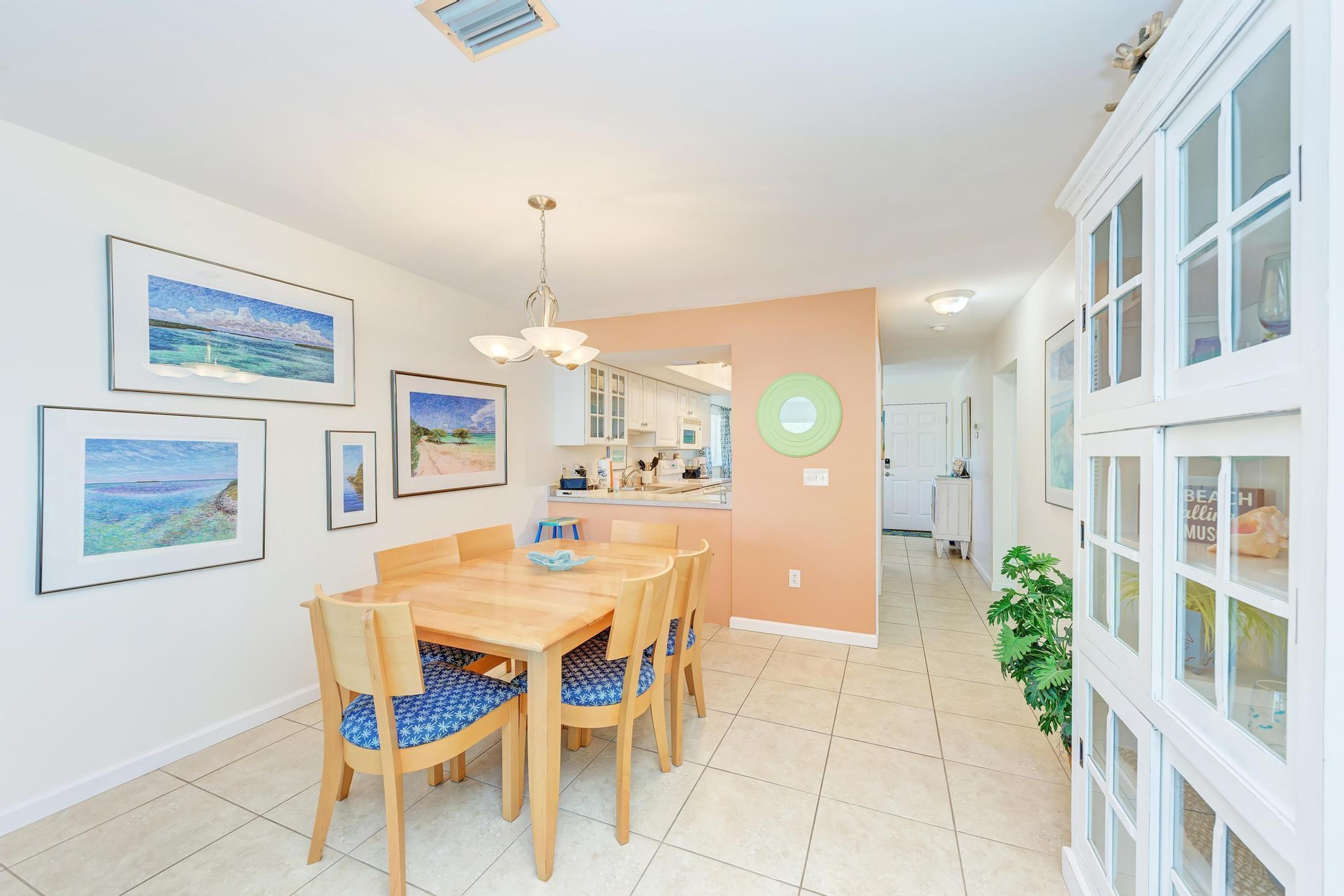 A dining area with a wooden table and chairs, a kitchen in the background, and a view of the sea through the windows.