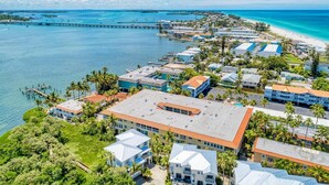 An aerial view of a coastal resort with multiple buildings, a pier extending into the water, and a beach in the background.