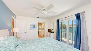 A bedroom with a bed, a ceiling fan, a window with curtains, and a view of the outside.